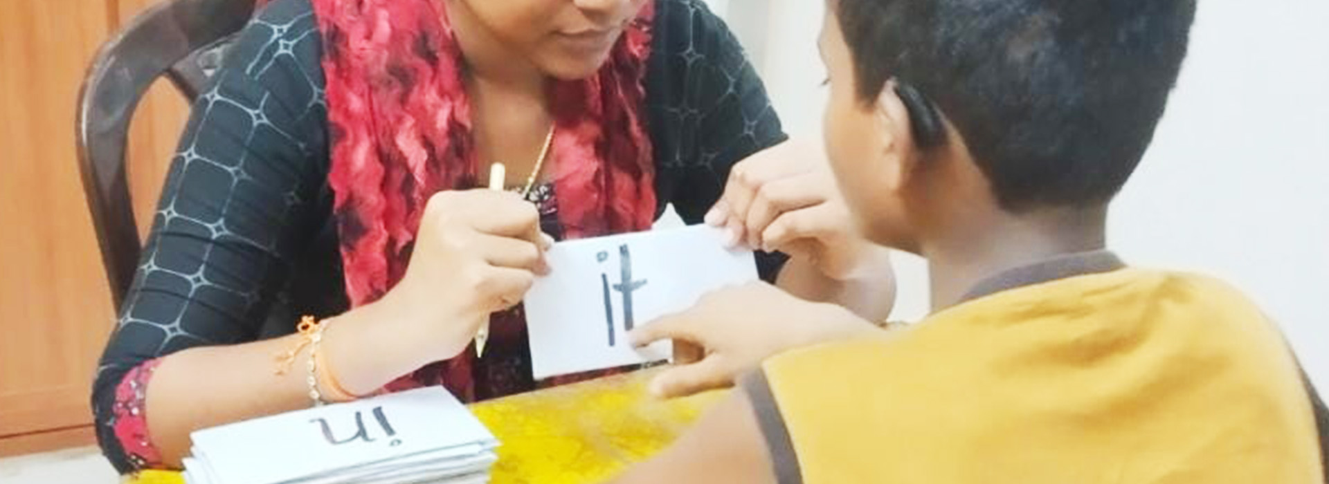 A speech therapist assisting a child in reading words by holding up a placard.