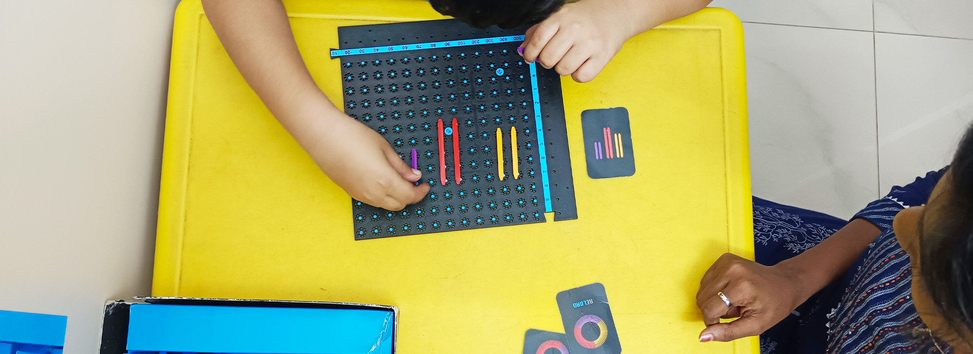 With the guidance of a speech therapist, children are enthusiastically engaged in the game of connecting dots of various colors, just like those on the small image cards provided. They are tasked with observing the color, shape, and length on each card, and then replicating it on a separate sheet of paper.